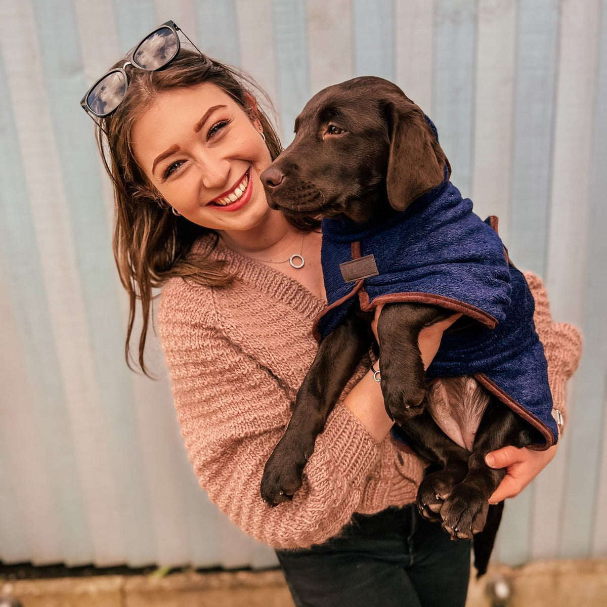 Smiling lady, holding a labrador puppy wearing a navy blue NASH bamboo dog drying coat. 
